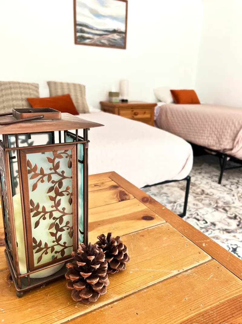 A carved lantern and pine cones on a wooden table beside a made bed