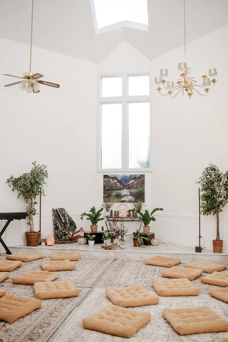 A tall white ceremony room with cushions set in a circle