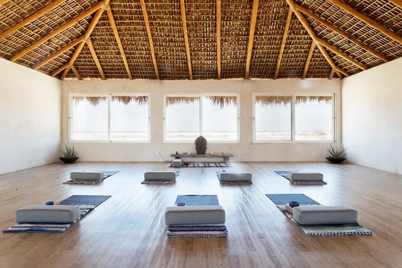 An open studio with a palm-thatch roof and mats on a wood floor