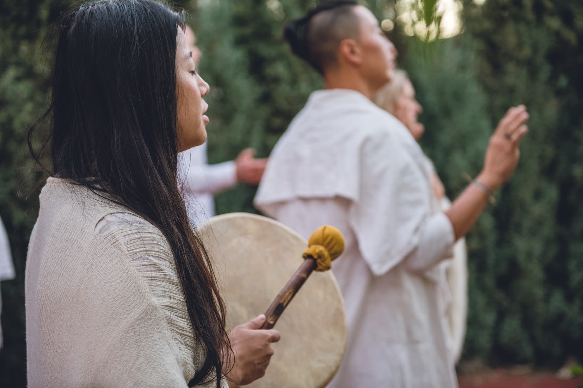 A woman holds a drum; a facilitator stands beside her in a white shirt